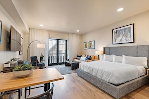 A hotel room with a large bed, a desk, a chair, a sofa, a dining table, and a view of the outside. - Gorgeous Condo|Juliette Balcony|Mountain & Village Views (Tamarack)