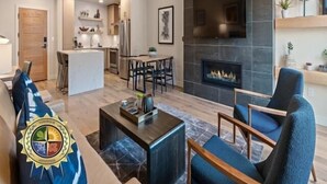 A modern living room with a fireplace, a dining area, and a kitchen in the background. - Polished Condo|Plaza and Mountain views (Tamarack)