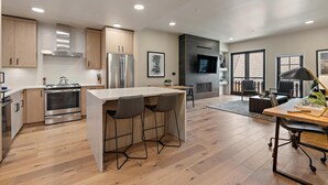 A modern kitchen with wooden cabinets, stainless steel appliances, and a central island with bar stools. - Polished Condo|Plaza and Mountain views (Tamarack)