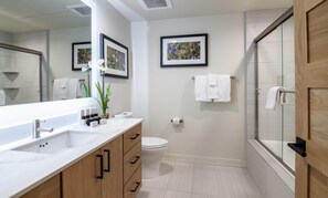 Une salle de bain moderne avec un grand miroir, un lavabo doté d’un plan de toilette en marbre, des meubles en bois, des toilettes et un espace douche.