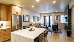 A modern kitchen with a large island, wooden cabinets, and a stainless steel refrigerator. - Modern Condo|Conveniently located (Tamarack)