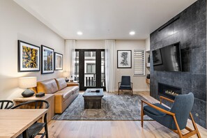 A modern living room with a sofa, coffee table, and a fireplace. There are framed pictures on the wall and a television mounted above the fireplace. - Impeccable Condo|Close to Dining Options (Tamarack)
