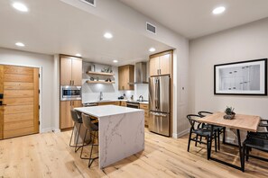 A modern kitchen with a central island, stainless steel appliances, and wooden cabinetry. - Impeccable Condo|Close to Dining Options (Tamarack)
