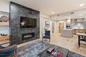 Una sala de estar moderna con chimenea, un televisor de pantalla plana y un comedor con una cocina al fondo.