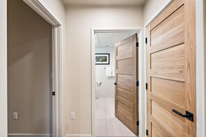 A hallway with a wooden door and a white door, leading to a bathroom with a toilet and a framed picture on the wall. - Impeccable Condo|Close to Dining Options (Tamarack)