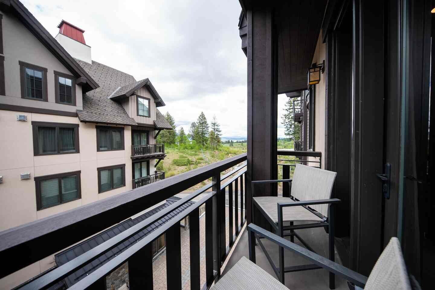 A balcony with a view of a residential area, a chair, and a door.