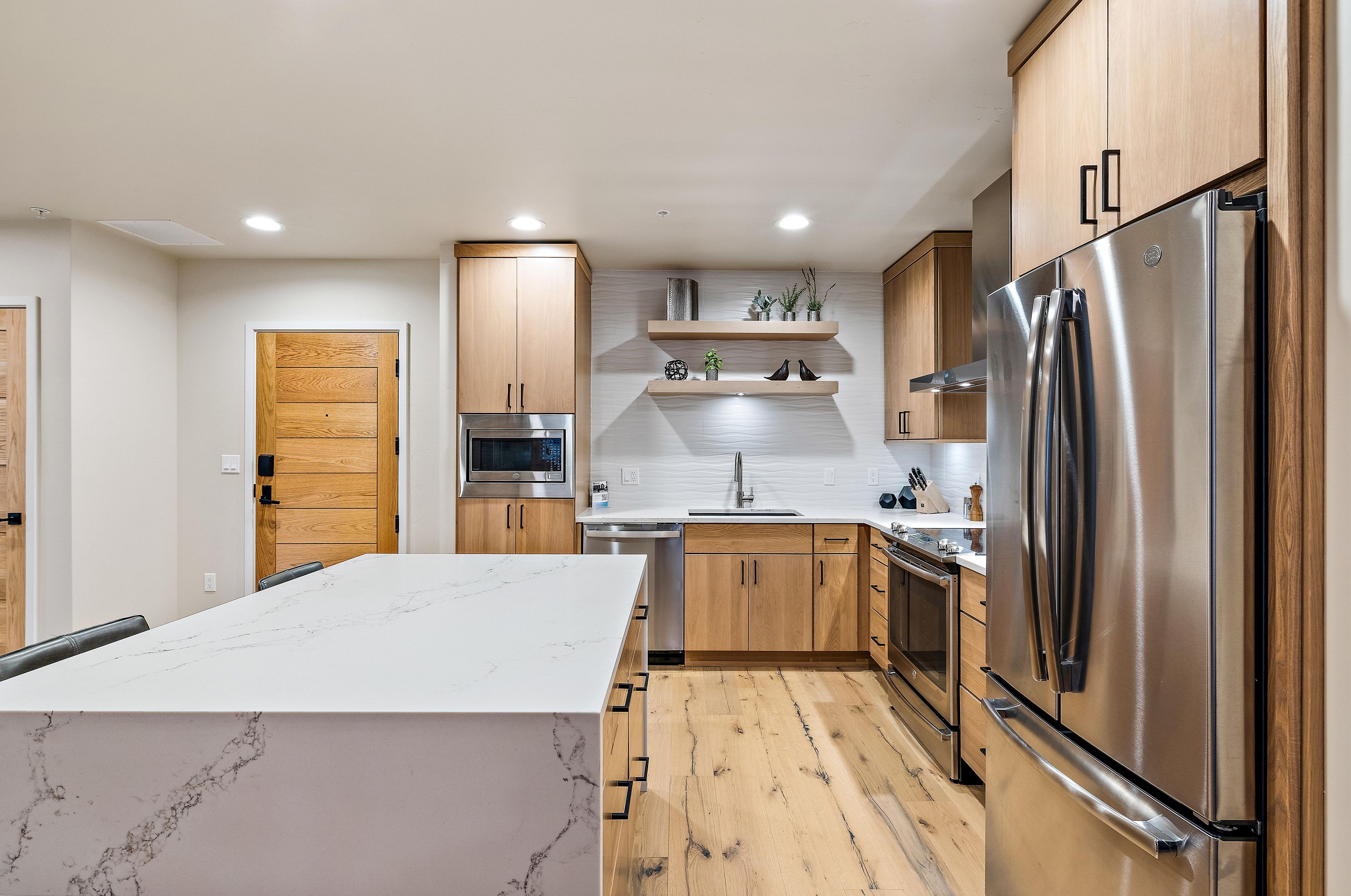 A modern kitchen with wooden cabinets, stainless steel appliances, and a marble countertop.