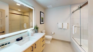 Une salle de bain moderne avec un grand miroir, des toilettes, une douche et un lavabo avec des placards.