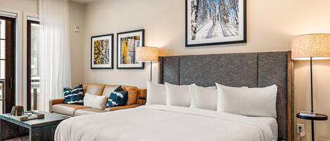 A hotel room with a large bed, a sofa, two framed artworks, and a floor lamp.