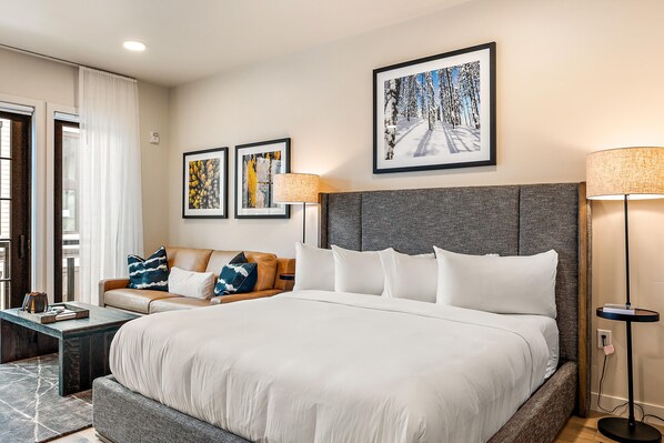 A hotel room with a large bed, a sofa, two framed artworks, and a floor lamp.
