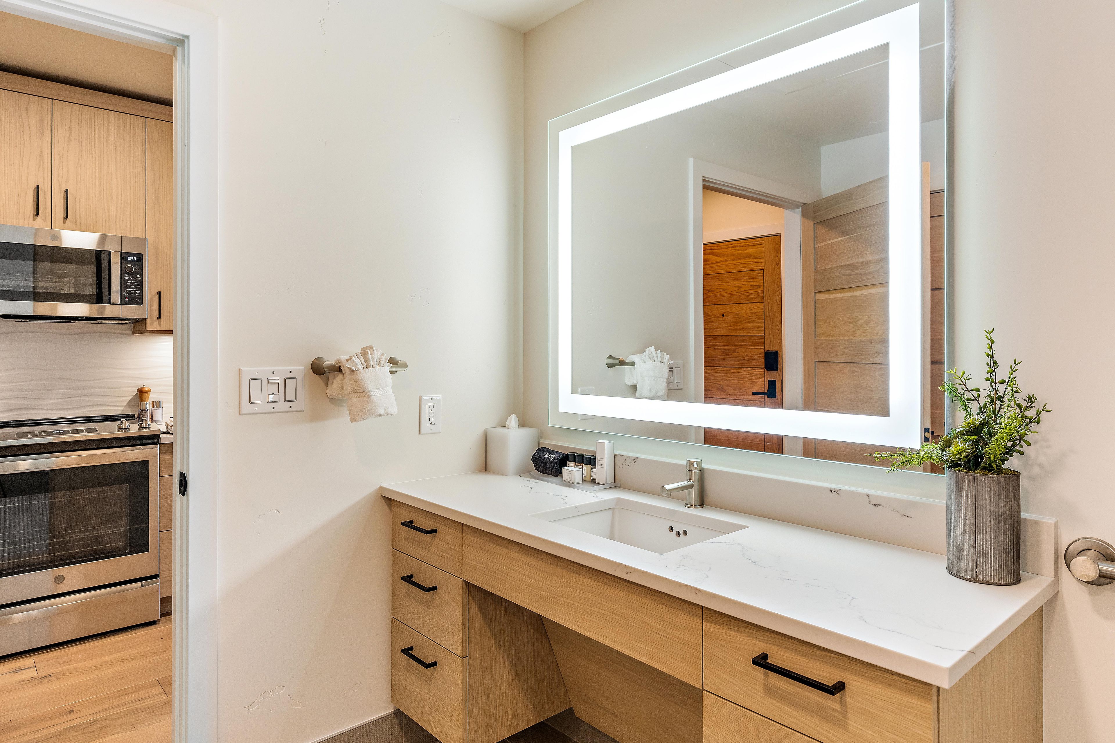 A modern bathroom with a large mirror, a sink, and a built-in oven.