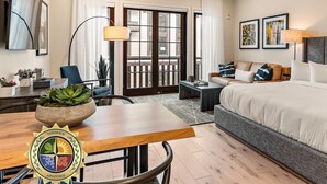 A hotel room with a bed, a desk with a plant, a chair, a sofa, and a large window. - Impeccable Condo|Pet Friendly|Juliette Balcony (Tamarack)