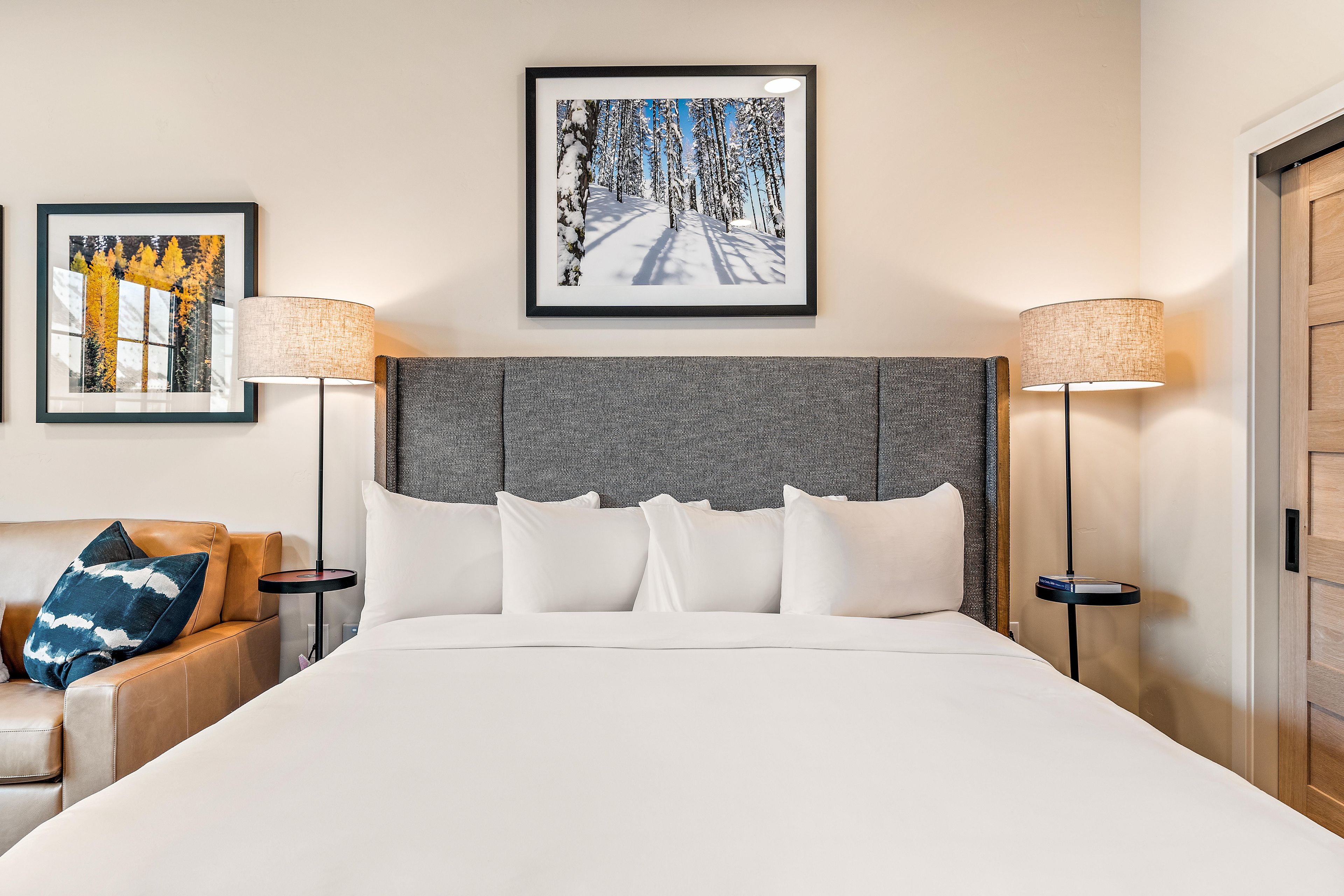 Une chambre d’hôtel avec un grand lit, deux tables de chevet avec des lampes, un canapé avec des coussins et deux œuvres d’art encadrées accrochées au mur.