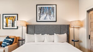 Une chambre d’hôtel avec un grand lit, deux tables de chevet avec des lampes, un canapé avec des coussins et deux œuvres d’art encadrées accrochées au mur.