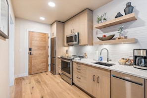 Een moderne keuken met houten kastjes, roestvrijstalen apparatuur en een wit aanrecht.