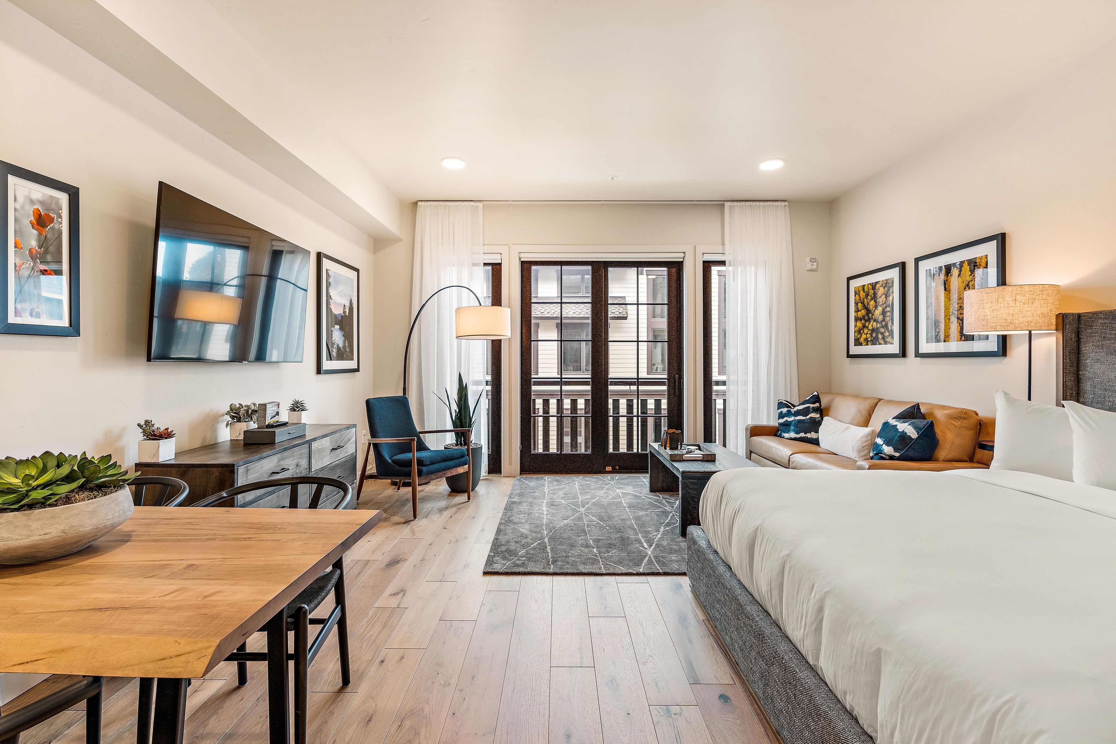 A modern hotel room with a bed, a desk, a chair, a sofa, and a dining table.