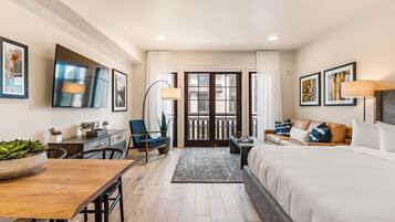 A modern hotel room with a bed, a desk, a chair, a sofa, and a dining table.