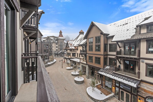A snow-covered town square with buildings featuring balconies and large windows.
