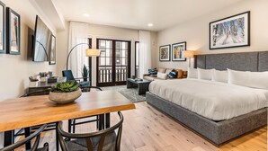 A hotel room with a bed, a desk, a chair, a table, and a window with curtains. - Impeccable Condo|Pet Friendly|Juliette Balcony (Tamarack)