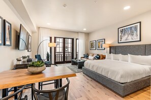 Habitación de hotel con cama, escritorio, silla, mesa y ventana con cortinas.