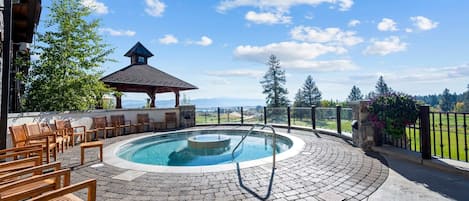A circular outdoor pool with a hot tub, surrounded by wooden chairs and a gazebo.