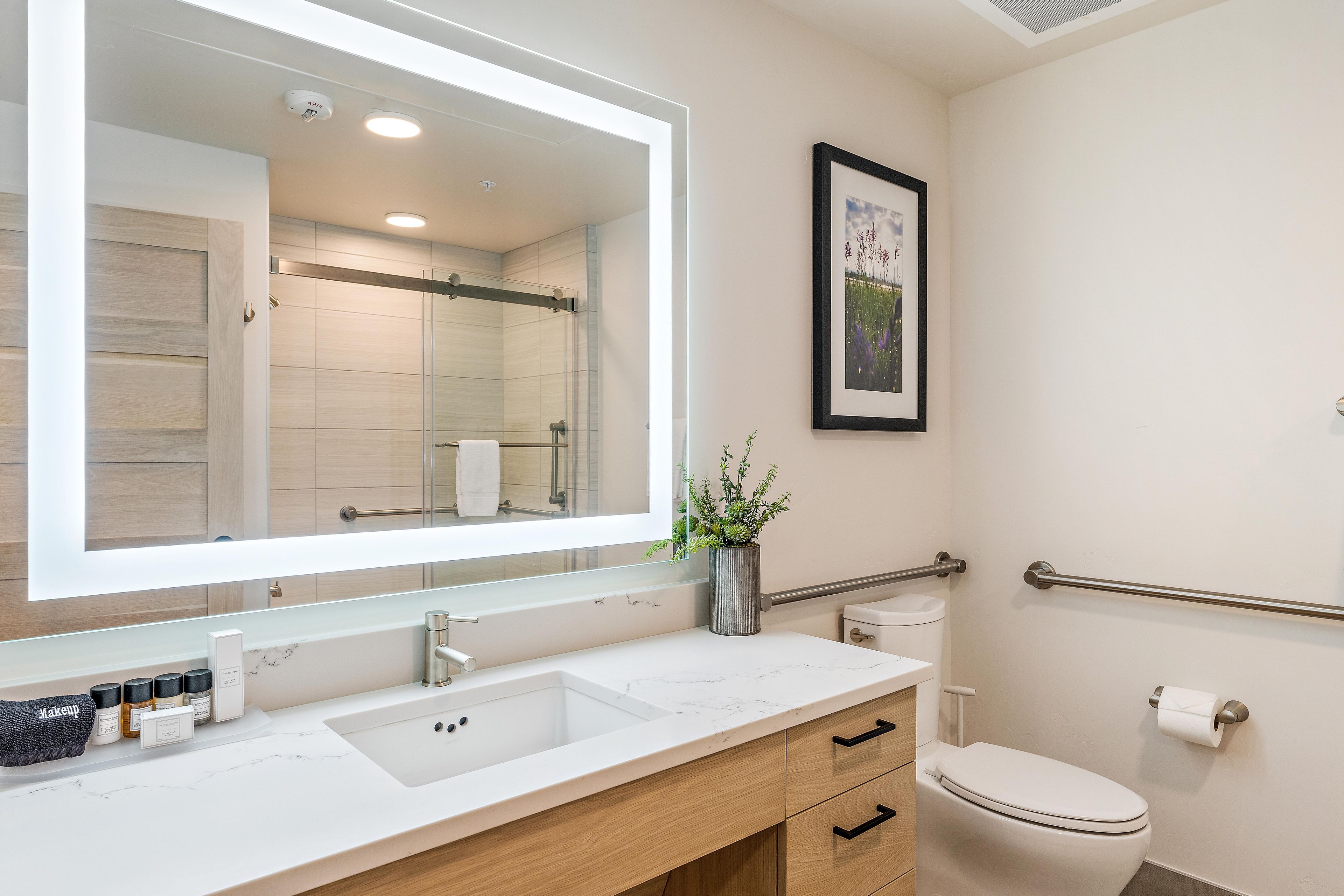 Een moderne badkamer met een grote spiegel, een wastafel, toilet en een lijst met een foto aan de muur.