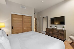 Une chambre avec un grand lit, une armoire en bois, une commode et un téléviseur fixé au mur.