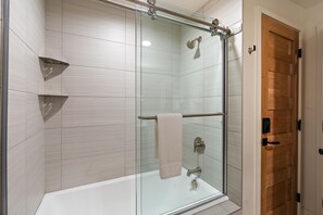 Une salle de bain moderne avec une douche à parois de verre, une baignoire blanche et une porte en bois.