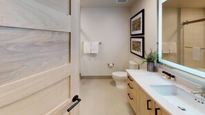 A modern bathroom with a wooden door, a white sink, a mirror, and a toilet.