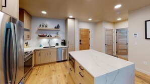 A modern kitchen with wooden cabinets, a stainless steel refrigerator, and a marble countertop. - Forest Haven | Includes Two 1-Day Lift Tickets (Tamarack)