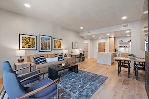 A modern living room with a sofa, coffee table, and chairs, a dining area with a table and chairs, and a kitchen in the background. - Four Rivers | Includes Two 1-Day Lift Tickets (Tamarack)
