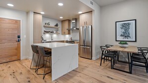 Een moderne keuken met een centraal eiland, roestvrijstalen apparatuur en een eethoek met een houten tafel en stoelen.