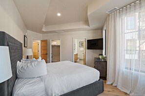 Een slaapkamer met een groot bed, een nachtkastje, een televisie en een badkamer zichtbaar door een open deur.