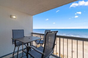 A balcony with a table and chairs, overlooking a beach. - Elegant & modern oceanfront escape- King bed, Pool (North Myrtle Beach)