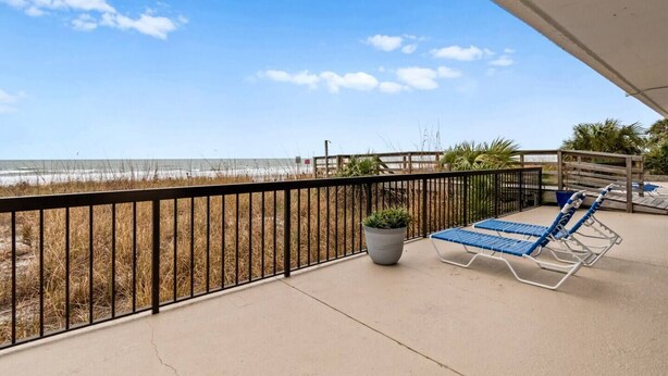 Un balcon avec vue sur la plage, une plante en pot et deux chaises longues.