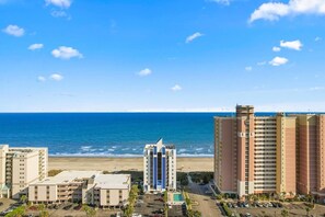 Ein Strandhotel mit Blick auf den Ozean, mehreren Parkplätzen und einem zentralen Gebäude mit blauen Akzenten.