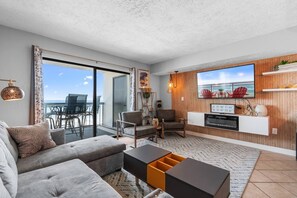 Een moderne woonkamer met een bank, stoelen, een salontafel en een televisie bevestigd aan een houten wand.