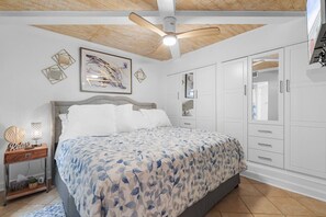 Ein Schlafzimmer mit einem Bett, einem Nachttisch, einem Deckenventilator, einem Kleiderschrank und einem gerahmten Kunstwerk an der Wand.