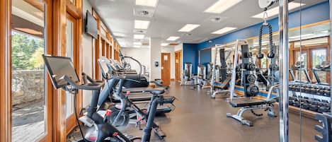 Un gimnasio con equipo de ejercicio, grandes ventanales y vistas al exterior.