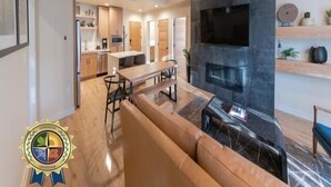 A modern living room with a fireplace, a dining area, and a kitchen in the background. - First Chair Lair | Includes Two 1-Day Lift Tickets (Tamarack)