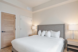 Una habitación de hotel con una cama grande, una puerta de madera, una mesita de noche y una lámpara.