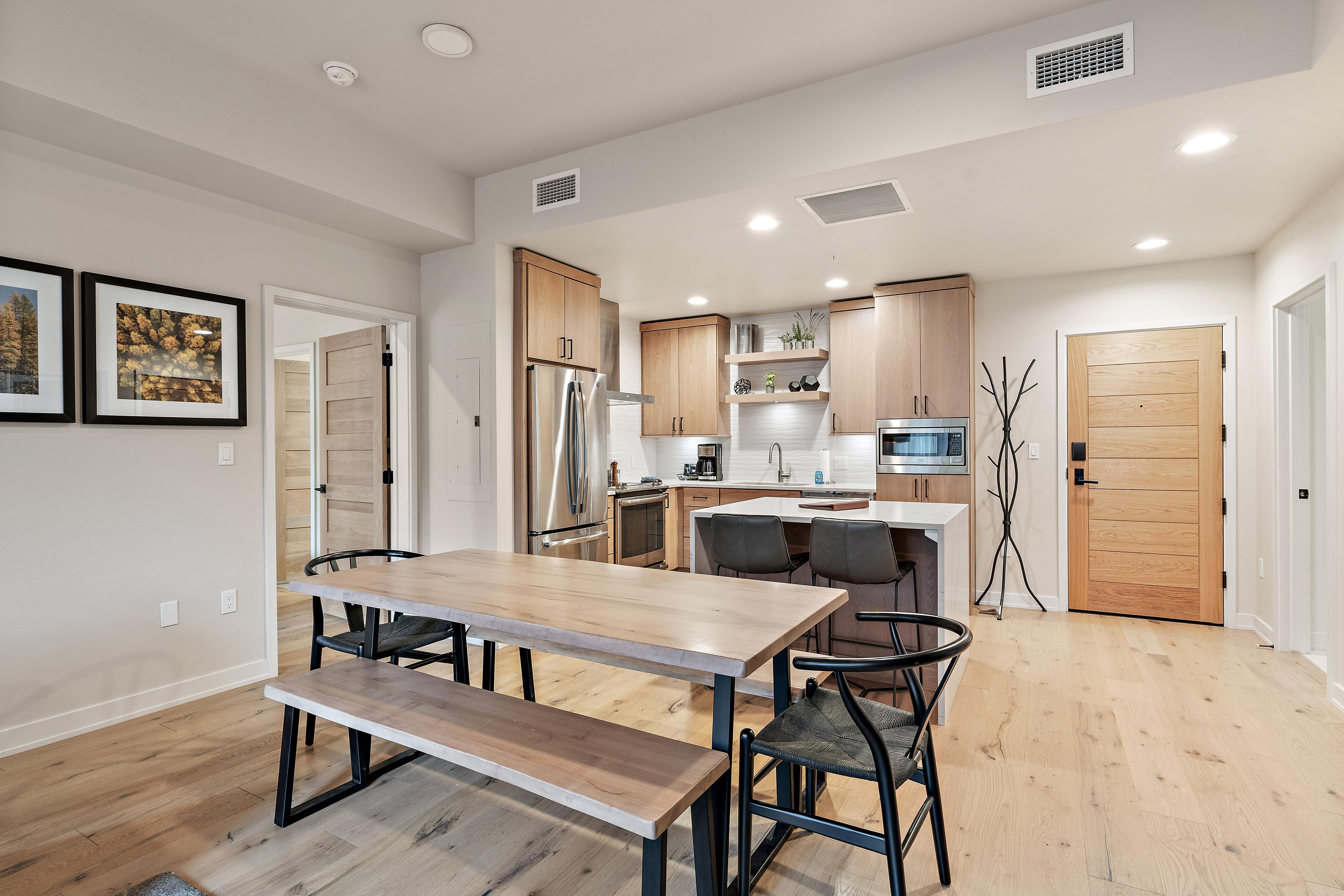 A modern kitchen with wooden cabinets, stainless steel appliances, and a dining area with a bench and chairs.