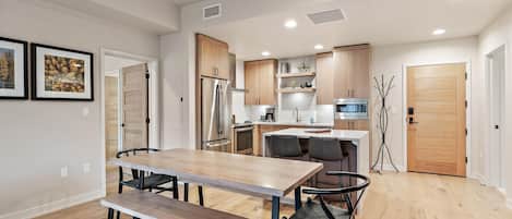 Une cuisine moderne avec des meubles en bois, des appareils en acier inoxydable et un coin repas comprenant une banquette et des chaises.