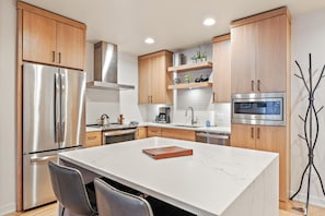 Cocina moderna con electrodomésticos de acero inoxidable, armarios de madera y encimera de mármol.