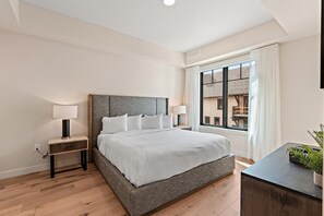 Un dormitorio moderno con una cama grande, mesitas de noche con lámparas, una ventana con cortinas y vistas al exterior.
