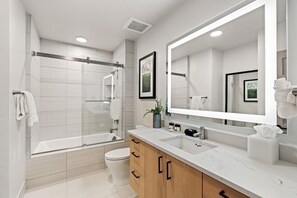 Un baño moderno con ducha de vidrio, un espejo grande y armarios de madera.