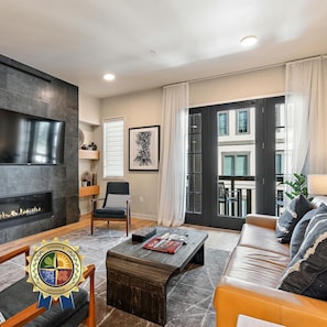 A modern living room with a fireplace, a sofa, a coffee table, and a large window with a view of the city. - Happy Aspen | Includes Two 1-Day Lift Tickets (Tamarack)