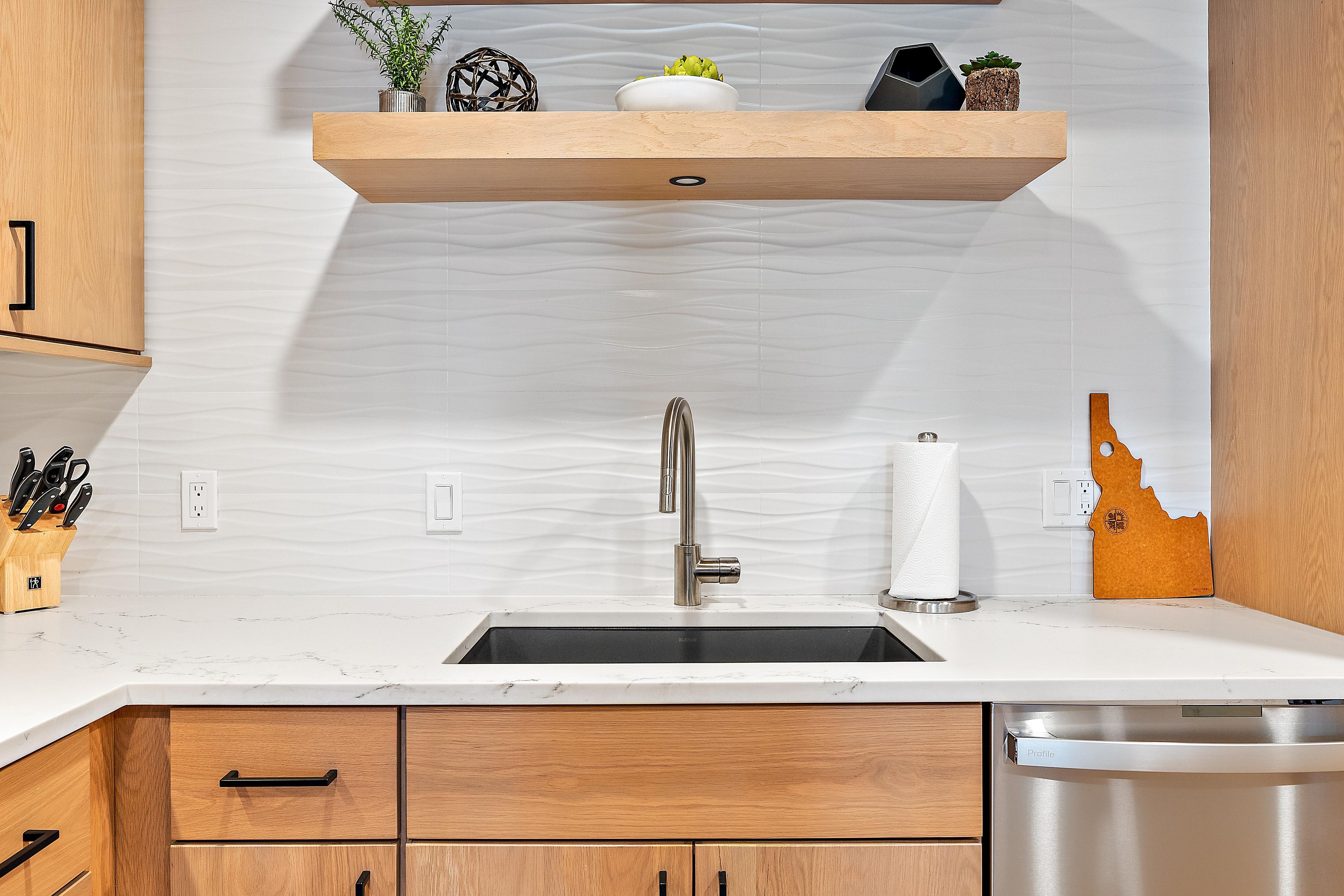 A kitchen with a stainless steel sink, wooden cabinets, and a marble countertop.