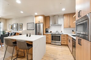 A modern kitchen with a central island, stainless steel appliances, wooden cabinets, and a marble countertop. - Happy Aspen | Includes Two 1-Day Lift Tickets (Tamarack)