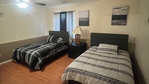 Une chambre avec deux lits, un ventilateur de plafond, une table de chevet avec une lampe et des œuvres d’art accrochées aux murs.